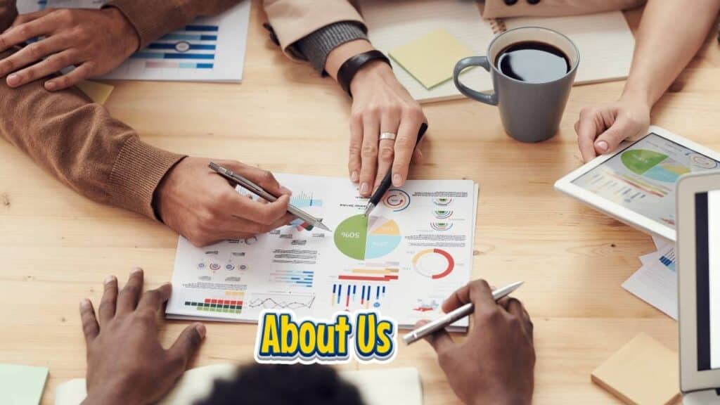 About Us page picture. People seated at a table, engaged with laptops and papers, collaborating on a project or discussion.